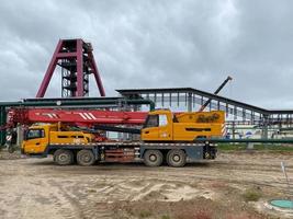 een groot geel vrachtauto kraan staat klaar naar werk Aan de bouw plaats van de nieuw fabriek foto
