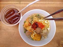 noodle soep, gemengd vlees ballen, met een rijk gearomatiseerd bouillon in een kop met een lepel Aan de houten tafel foto