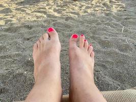 vrouw poten, voeten met een mooi rood pedicure Aan de achtergrond van zand Aan vakantie Aan de strand in een warm tropisch oostelijk paradijs land zuidelijk toevlucht foto