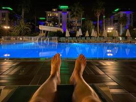 Mannen voeten Aan een zon ligstoel door de zwembad Bij nacht in een hotel in een warm oostelijk tropisch land zuidelijk paradijs toevlucht foto