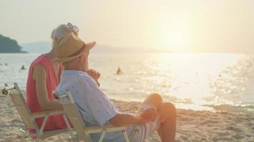 twee ouderen mannen en Dames zitten stoel Bij de strand pratend en aan het kijken de zon en de zee Aan hun zomer vakantie en ze glimlach en genieten hun vakantie. foto