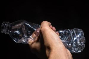 hand met een plastic fles op zwarte achtergrond foto