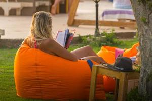 jong vrouw zit Aan een strand lounge en leest een boek Aan vakantie foto