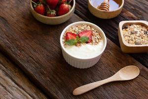 aardbei yoghurt in een houten kom met muesli, honing, munt en vers aardbei Aan houten achtergrond. Gezondheid voedsel concept. foto