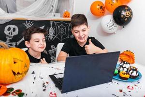 gelukkig jong jongens, broers pratend met grootouders of vrienden via video telefoontje gebruik makend van laptop Aan halloween dag , opgewonden jongens in kostuums op zoek Bij computer tonen duimen omhoog foto