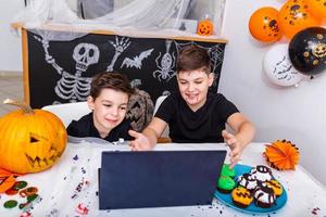 gelukkig jong jongens, broers pratend met grootouders via video telefoontje gebruik makend van laptop Aan halloween dag , opgewonden jongens in kostuums op zoek Bij computer golvend en lachend. foto