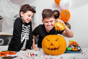 twee jongens, broers in kostuums zijn op zoek wat is binnen van jack O' lantaarn halloween pompoen Aan de tafel. gelukkig halloween foto