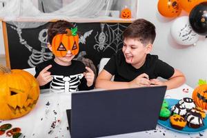 gelukkig jong jongens, broers pratend met grootouders via video telefoontje gebruik makend van laptop Aan halloween dag , opgewonden kind tonen zijn nieuw masker voor halloween Aan camera foto