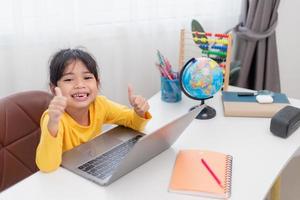 Aziatisch weinig meisje Bij huis aan het doen huiswerk foto