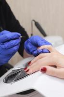 meester in beschermende handschoenen tijdens een manicure bij schoonheidssalon. meester-manicurist vernist de marsala-gel op de nagels van een vrouwelijke cliënt. het concept van schoonheid en gezondheid. foto