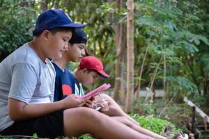 drie Aziatisch jongens lezing vogelstand details en gaan naar gebruik kijker naar kijk maar vogelstand Aan de bomen gedurende zomer kamp, idee voor aan het leren schepsels en dieren in het wild dieren buiten de klas. foto