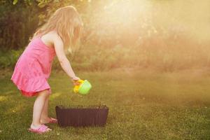 schattig weinig meisje gieter bloemen in de zomer tuin foto