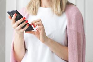 dichtbij omhoog vrouw handen met rood manicure gebruik een smartphone Aan wit achtergrond schrijven tekst bericht genieten online communicatie boodschappen doen bestellen Product foto