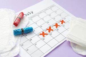 menstruatie- stootkussens en tampons Aan menstruatie periode kalender met rood kruis merken leugens Aan lila achtergrond foto