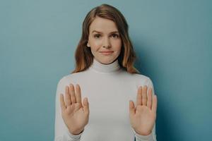 aantrekkelijke jonge gefocuste vrouw die een stopgebaar toont, nee zegt, geïsoleerd over blauwe studioachtergrond foto