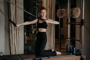 fit slank vrouw Aan pilates hervormer glimlachen gedurende uitrekken opdrachten foto