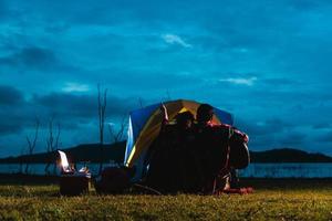 tent zorgeloos paar ontspannende afgelegen reizen concept - romantisch Aziatisch paar toeristen zittend Bij een kampvuur in de buurt tent, knuffelen elk andere onder bomen en nacht lucht. nacht camping foto
