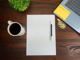 vlak leggen, bespotten omhoog papier. werkruimte in de achtergrond van de kantoor bureau van de top visie. met blanco wit papier, laptops, kantoor benodigdheden, potloden, groen bladeren, en koffie cups in een houten tafel. foto