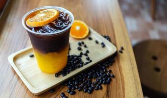 bevroren koffie drinken menu oranje americano met vers oranje fruit gemengd in een plastic kop Aan de houten bar teller in de cafe foto