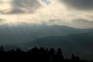 de zon schijnt door de wolken bovenstaand de bergen foto