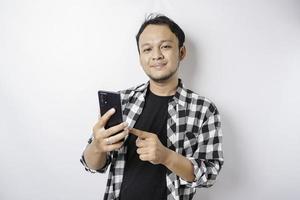een portret van een gelukkig Aziatisch Mens is glimlachen terwijl Holding Aan zijn telefoon, geïsoleerd door wit achtergrond foto