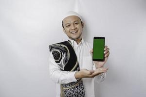 een portret van een gelukkig Aziatisch moslim Mens glimlachen terwijl tonen kopiëren ruimte Aan zijn telefoon, geïsoleerd door wit achtergrond foto