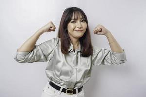 opgewonden Aziatisch vrouw vervelend een salie groen overhemd tonen sterk gebaar door hijs- haar armen en spieren glimlachen trots foto