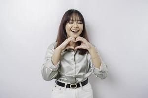 een aantrekkelijk jong Aziatisch vrouw vervelend een salie groen overhemd voelt gelukkig en een romantisch vormen hart gebaar drukt uit inschrijving gevoelens foto