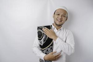 een portret van een gelukkig Aziatisch moslim Mens met gebed tapijt Aan zijn schouder is glimlachen geïsoleerd door wit achtergrond foto