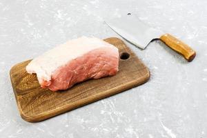 rauw besnoeiing van varkensvlees schouder Aan bord met mes of keuken bijl. hakmes met vers rauw vlees Aan grijs beton achtergrond foto
