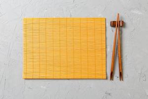 twee sushi eetstokjes met leeg bamboe mat of hout bord Aan steen achtergrond top visie met kopiëren sta foto