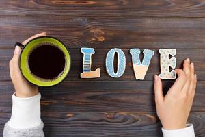 vrouw handen met koffie en hart vormig koekjes Aan houten tafel, top visie. liefde concept. koekjes liefde brief foto