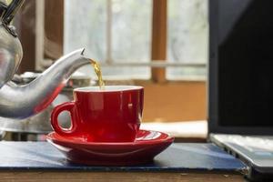 een rood koffie kop is geplaatst Aan de bureau. kantoor of Bij huis met een notitieboekje computer toetsenbord tablet pc foto