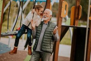 opa uitgeven tijd met zijn kleindochter in park speelplaats Aan herfst dag foto