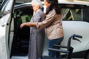 verzorger helpt aziatische bejaarde vrouw met een handicap om in haar auto te stappen, medisch concept. foto