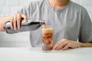 jong vrouw gieten verkoudheid cola zacht drinken Frisdrank van een fles in een glas in haar hand. Gezondheid zorg, gezond eetpatroon levensstijl concept. foto