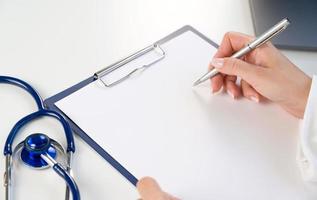 medisch sjabloon voor tekst. detailopname van dokter handen Holding pen Aan papier tablet met stethoscoop in de buurt foto