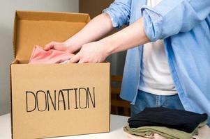 mannetje vrijwilliger zet kleren in bijdrage doos. karton doos met kleren voor liefdadigheid. helpen armen.delen sociaal werkzaamheid. foto