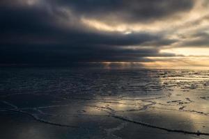 Baltisch zee kust met steentjes en ijs Bij zonsondergang foto