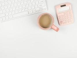 vlak leggen van computer toetsenbord, roze kop van koffie en roze rekenmachine Aan wit achtergrond met kopiëren ruimte. foto