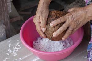 hand- van ouderen vrouw zittend naar rooster de kokosnoot naar koken. foto