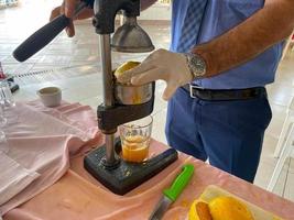 de werkwijze van maken vers geperst geel oranje sap, een Mens knijpt sap in een glas met zijn handen in een hotel in een warm oostelijk tropisch land zuidelijk paradijs toevlucht foto