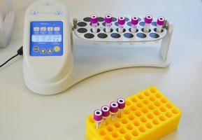 een wetenschapper in een laboratorium plaatsen test buizen met bloed of urine in de houder van een thermisch analysator. modern medisch geautomatiseerd uitrusting foto
