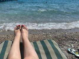 mooi poten van een vrouw met een pedicure hebben een rust uit Aan een zon ligstoel Aan de strand door de zee foto