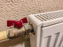 radiator voor leveren verwarming naar woon- appartementen. wit accu met een rood kraan voor aanpassen de druk van heet water. tegen de backdrop van een gepleisterd muur foto
