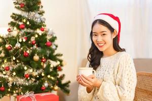 Kerstmis viering concept, Aziatisch vrouw zit Aan stoel in de buurt Kerstmis boom en Holding koffie kop