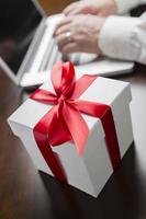 wit geschenk doos met rood boog in de buurt Mens gebruik makend van laptop foto