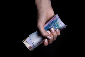 twee handen met hryvnia's. detailopname vrouw hand- geven geld voor iets met geïsoleerd Aan zwart achtergrond, tellen, betalen, boodschappen doen met hryvnia's, corruptie, tellen grivna's bankbiljetten Oekraïne foto