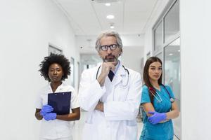 detailopname voorkant visie van groep van gemengd leeftijd artsen en verpleegsters staand kant door kant en op zoek Bij de camera. senior mannetje dokter is staand in voorkant net zo een leider. foto