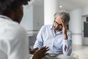 Afrikaanse Amerikaans dokter pratend naar een geduldig wie is klagen van hoofdpijn Bij de ziekenhuis medisch kliniek. dokter en geduldig bespreken over- verslag doen van in ziekenhuis aan het wachten kamer foto